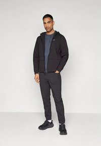 Črno jakno s kapuco čez sivo majico, kombinirano s črnimi hlačami in supergami. Opremljena z zadrgo spredaj in žepi. Gladek, lahek material.