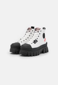 Zapatillas altas blancas con puntera de goma negra y suela gruesa. Presenta acentos en negro y rojo, diseño de cordones y logo en el lateral.