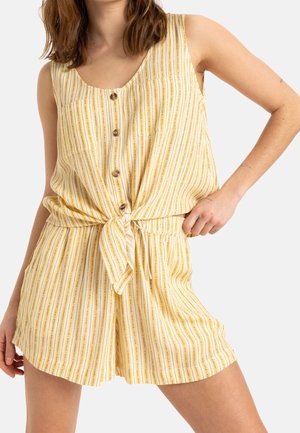 Femme portant un haut sans manches rayé jaune et blanc, boutonné et noué à la taille avec un short taille haute assorti.