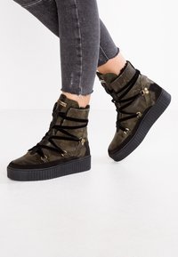 Baskets montantes en camouflage noir et vert olive avec une épaisse semelle en caoutchouc noir, dotées de lacets noirs et d'accents en métal doré.
