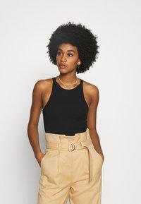 Top de alças largas preto com estrutura canelada, combinado com calças beje de cintura alta com uma grande fivela de cinto em forma de anel prateado.