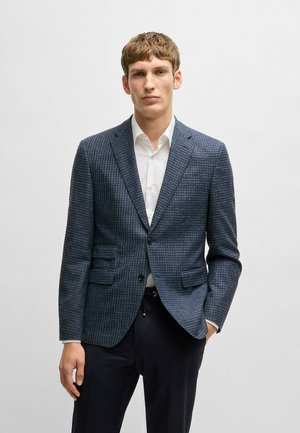 Navy blue checked blazer with notched lapels, two front pockets, single-button closure, and textured fabric. Paired with a white shirt.