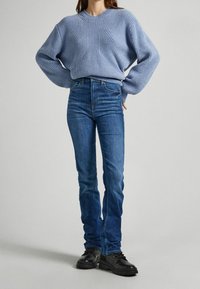 Jersey de punto azul claro con un patrón texturizado, combinado con unos vaqueros de talle alto azul oscuro y botas negras con cordones.