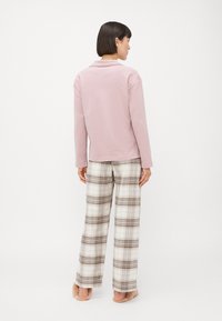 Ljusrosa långärmad topp med krage i kombination med lösa, rutiga pyjamabyxor i kräm, brunt och grått. Mjuk tyg och avslappnad passform.