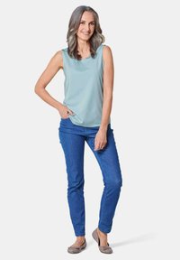 Top senza maniche azzurro abbinato a jeans blu slim-fit e ballerine grigie. Il top presenta una texture liscia e un collo rotondo.