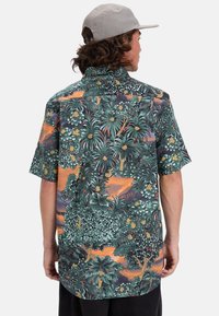 Camisa de manga corta con un vibrante estampado botánico de follaje verde, detalles en naranja y cuello estándar. Fabricada en un tejido ligero.