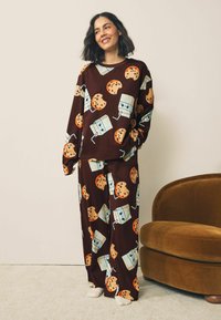 Brown pajama set featuring a playful cookie and milk carton pattern. The top has long sleeves, and pants are loose-fitting with a ribbed texture.