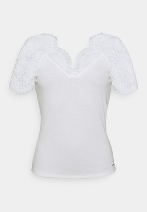 Bílý přiléhavý top s hlubokým výstřihem do V; krátké krajkové rukávy s vlnitými okraji. Hladká textur kůže, zdůrazňující jemné krajkové detaily.