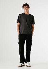 Tricou gri închis cu guler rotund, cu o croială lejeră, asortat cu pantaloni cargo negri cu buzunare laterale și adidași albi cu talpă bej.