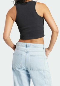 Kvinna iklädd en svart ärmlös crop top och ljusblå högmidjade denimjeans med stora bakfickor, stående med händerna på höften.