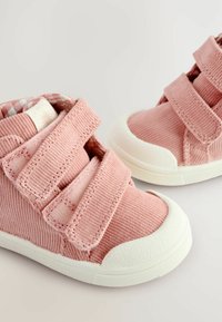 Rosa Corduroy High-Top-Schuhe mit weißen Gummisohlen und Klettverschlüssen. Innenraum mit einem gemusterten Stofffutter.