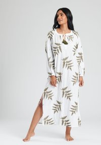Vestido maxi blanco con estampado de helechos verdes, mangas largas y escote con lazo. Presenta aberturas laterales para facilitar el movimiento. Tejido ligero.