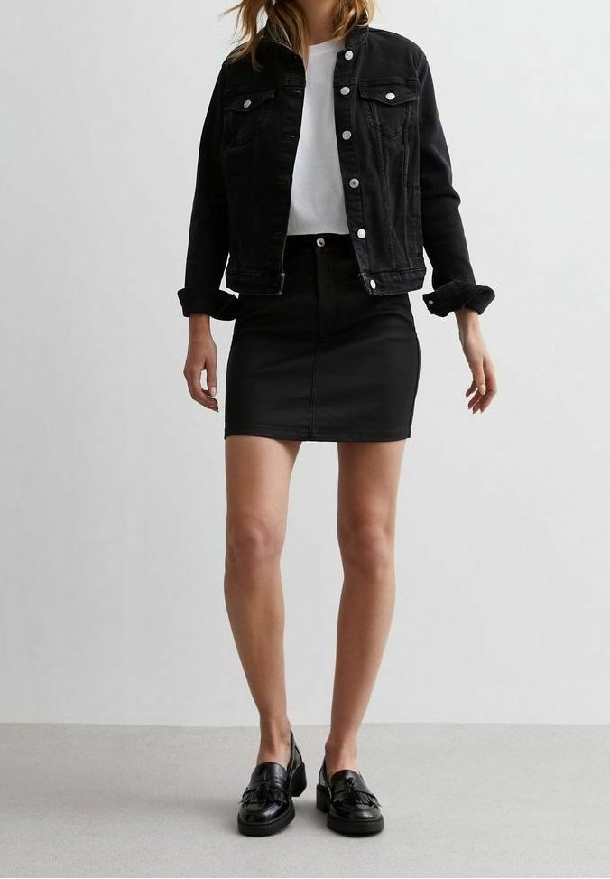 Veste en denim noir avec boutons argentés, t-shirt blanc, jupe en cuir noire et mocassins noirs. Design simple avec peu de détails.
