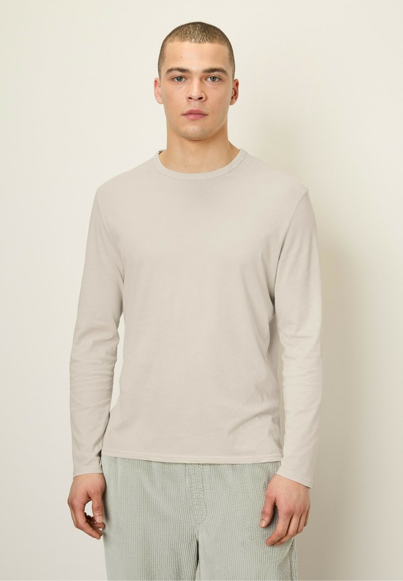 Svetlo béžová košeľa s dlhým rukávom a okrúhlym výstrihom. Hladká textúra, bežný strih. Nosí sa s svetlozelenými kordurovými nohavicami.