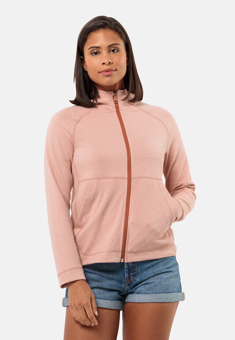 Giacca zip-up rosa chiaro con un motivo testurizzato, colletto alto e zip marrone a contrasto, abbinata a pantaloni corti di denim.