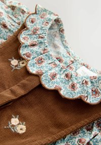 Bruine ribfluwelen jurk met een bloemenblauwe kraag met golfranden en geborduurde details op het lijfje. Getextureerde stof, ingewikkelde patronen.