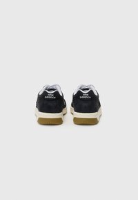 Sorte semsket og mesh sneakers med hvite detaljer, med gummisåle og "new balance"-logo på hælen, bakfra.