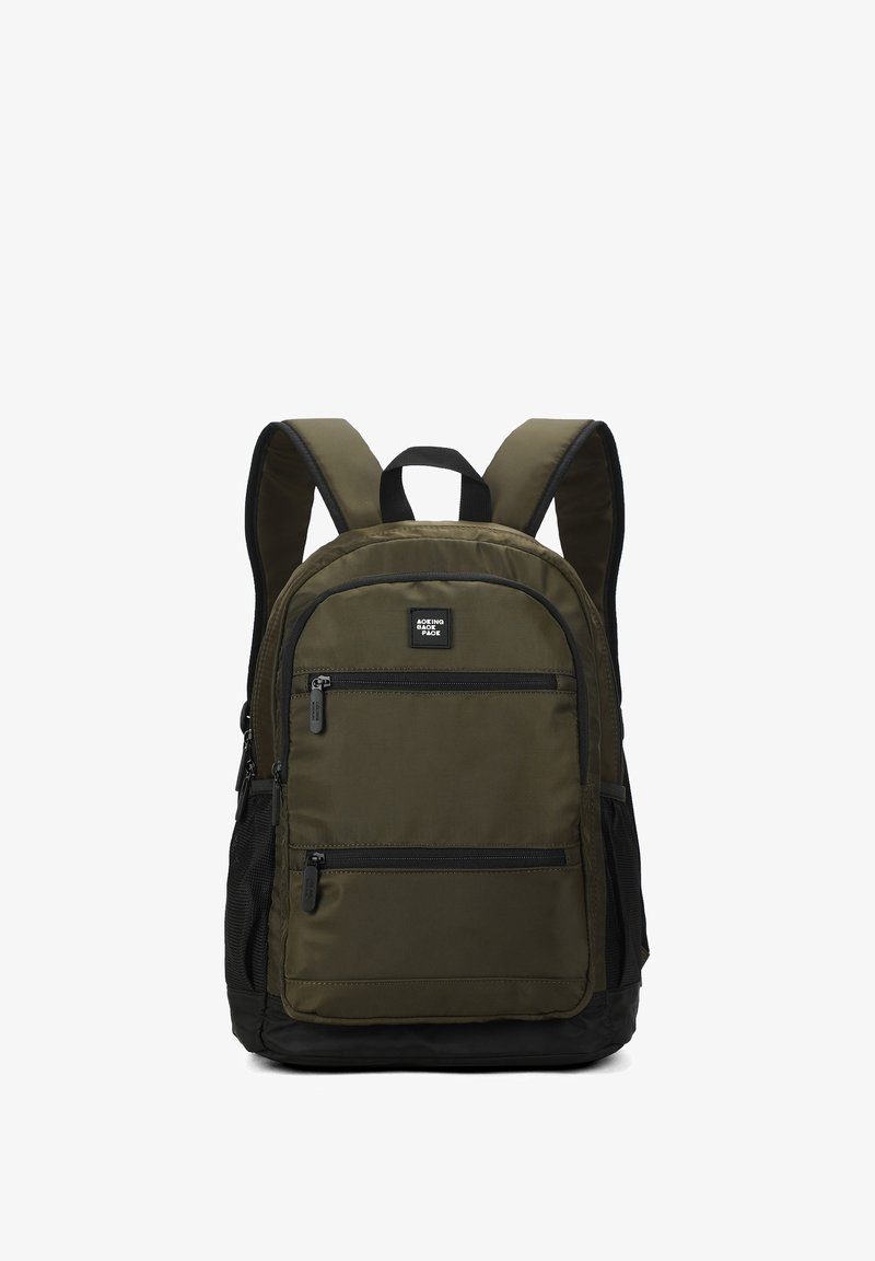 Sac à dos vert olive avec accents noirs, deux poches avant zippées, poches latérales en mesh, bretelles rembourrées et une poignée supérieure pour le transport.