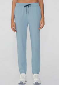 Jasnoniebieskie dresy z mieszanki bawełny, z elastycznym pasem ze sznurkiem ściągającym i zwężanymi mankietami. Noszone z białymi trampkami.