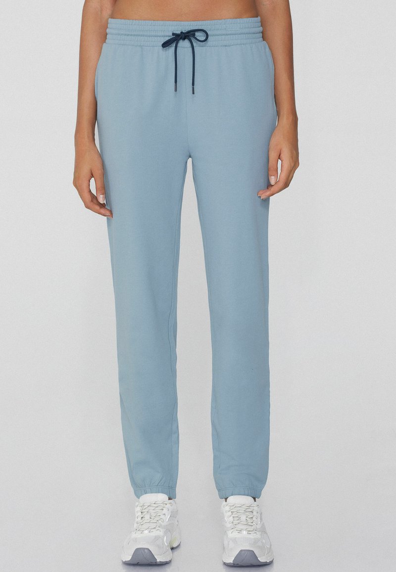 Jasnoniebieskie dresy z mieszanki bawełny, z elastycznym pasem ze sznurkiem ściągającym i zwężanymi mankietami. Noszone z białymi trampkami.