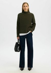 Tamnozelena rebrasta turtleneck pulover, uparen s visokim tamnim trapericama i crnom torbicom. Obuća ima šiljaste vrhove.