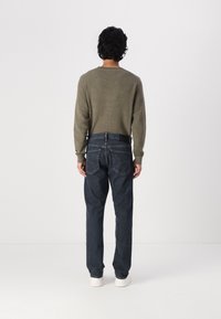 Lys olivengrønn genser med lange ermer, sammen med mørkeblå straight-leg jeans. Antrekket er fullført med hvite sko, med fokus på bakvinkel.