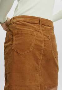 Mini gonna in corduroy marrone con doppie tasche posteriori e tessuto testurizzato, con un leggero svasamento all'orlo.