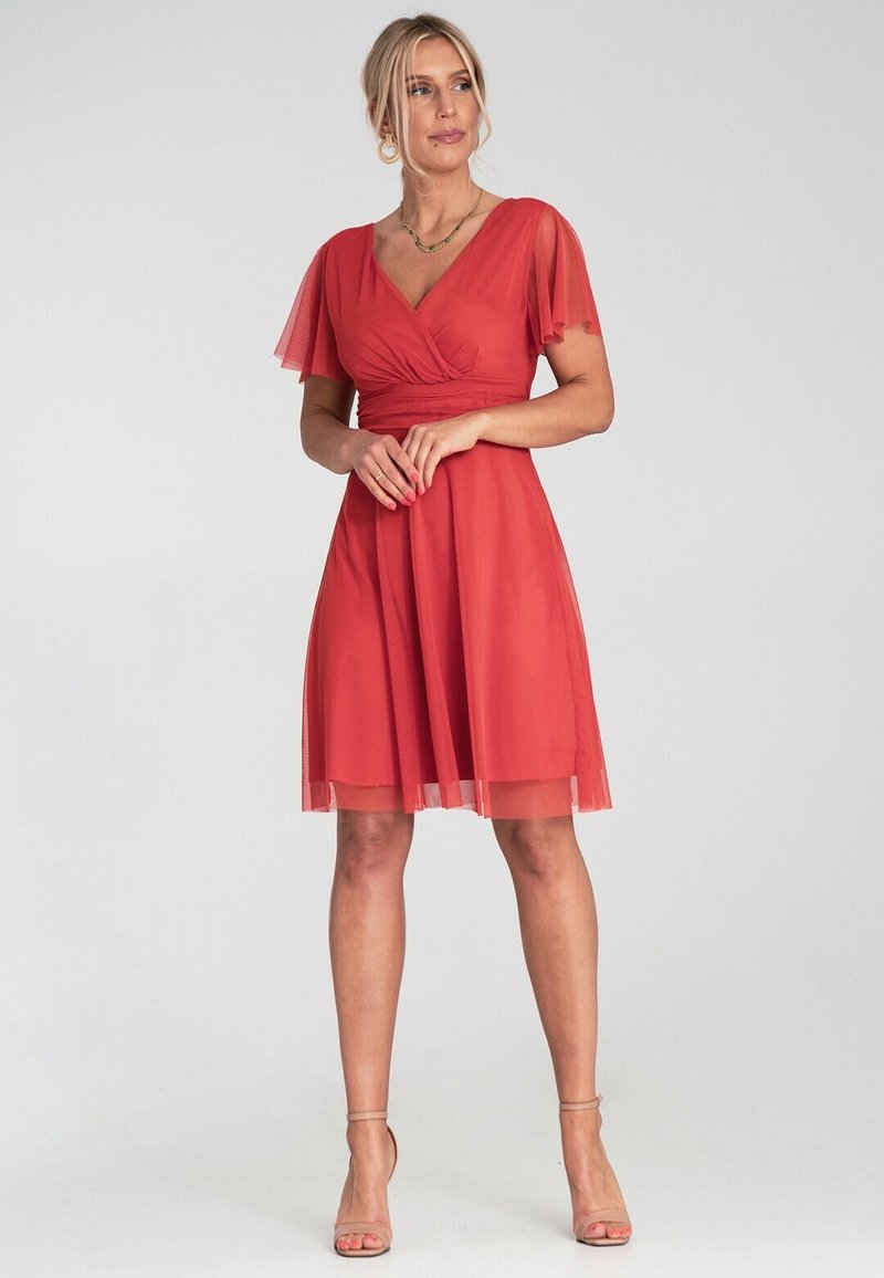 Rotes knielanges Kleid mit kurzen Schmetterlingsärmeln, einem V-Ausschnitt und einem taillierten Oberteil. Der durchsichtige Überwurf und der fließende Rock erzeugen Bewegung.