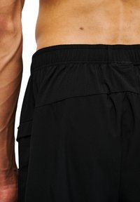 Schwarze Sportshorts mit strukturiertem Bund und seitlichen Taschen, aus leichtem, feuchtigkeitsableitendem Material hergestellt.