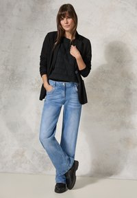 Svart kavaj över en texturerad svart tröja, i kombination med ljusblå vida jeans och svarta skor. Outfiten har en modern avslappnad stil.