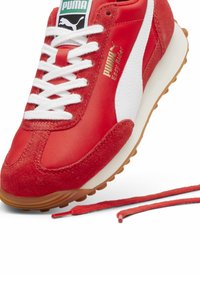 Röd mocksneaker och nylon med vita accenter, platta snören och sula av gummigummi. Har "PUMA Easy Rider"-logga på sidan.