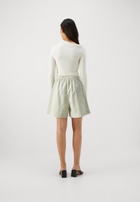 Light green striped shorts with an elastic waistband, paired with a fitted cream top and black block-heeled shoes. Smooth texture.