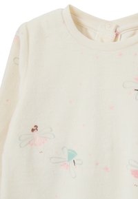Sudadera de forro polar color crema con diseños bordados de hadas, con acentos en tonos pastel y pequeños puntos rosas por doquier. Cierre de botones en la parte posterior.