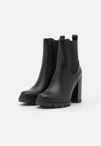 Botas de tobillo de cuero negro con paneles elásticos laterales, suelas de goma gruesas y tacones altos en bloque. Presentan una textura suave y un diseño elegante.