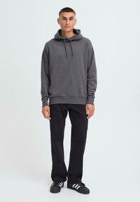 Grijze hoodie met trekkoorden, ribbelzoom, gecombineerd met zwarte broek en zwarte sneakers met witte strepen. Glad materiaal, ontspannen pasvorm.