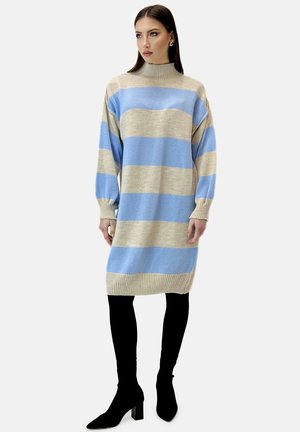 Strikket kjole med beige og lyseblå vandrette striber, høj hals, lange ærmer og en afslappet pasform, kombineret med sorte strømpebukser og hæle.