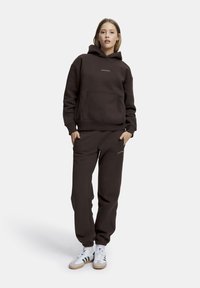Brun hoodie med ficka fram och logotyp, i kombination med matchande joggers. Avslutad med vita sneakers med gröna ränder. Slät textur.