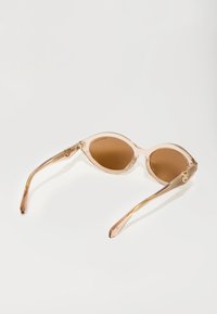 Ochelari de soare transparenti, de culoare roz deschis, cu formă cat-eye, având lentile maronii, cu brațe subțiri și accente aurii subtile pe laterale.