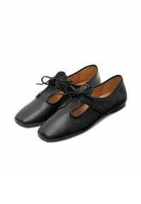 Chaussures en cuir noir à bout carré, dotées de découpes et de nœuds liés. L'intérieur est de couleur beige, offrant un contraste avec l'extérieur.