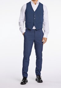 Námořnická vesta a padnoucí kalhoty z texturované tkaniny, doplněné bílou košilí. Černé společenské boty dotvářejí celý outfit.