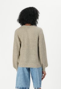 Beige gebreide trui met een losse pasvorm, lange mouwen en ribbelstructuur, gecombineerd met lichtblauwe denim shorts.
