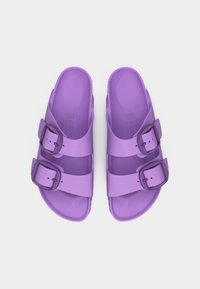 Ζευγάρι μωβ σανδάλια με δύο ρυθμιζόμενους ιμάντες με αγκράφες, φαίνετ αι από πάνω σε λευκό φόντο.