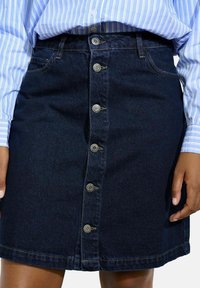 Temna denim krila s ravnim krojem, ki ima spredaj vrsto šestih kovinskih gumbov, dve stranski žepi in rumene šive.