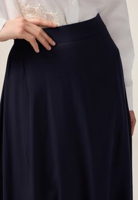 Jupe marine avec une texture lisse, taille haute et design plissé ; comporte des détails délicats à la taille, associée à une blouse blanche.