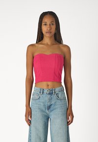 Pieguļošs strapless tops spilgti rozā tekstūrētā audumā ar sirds formas kakla izgriezumu un īsā dizainā, apvienots ar gaiši ziliem augstās jostasvietas džinsiem.