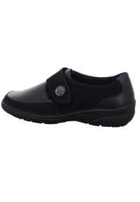 Black shoe with a smooth leather toe and soft suede body, featuring a round metal accent and a Velcro strap for easy fastening.