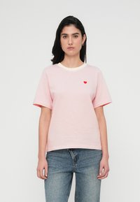 Ριγέ μπλουζάκι σε ανοιχτό ροζ με κρεμ λαιμόκοψη, διαθέτοντας κοντά μανίκια και μια μικρή κόκκινη καρδιά κεντημένη στο στήθος.