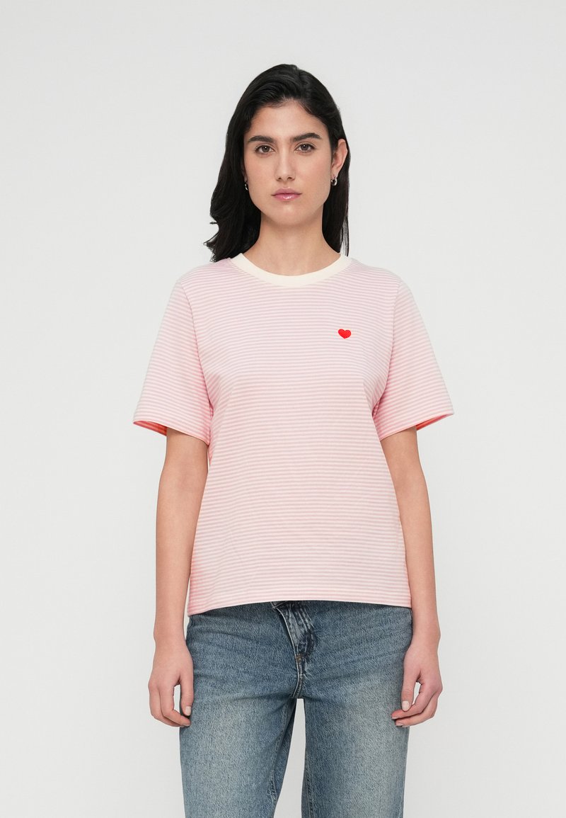 Ριγέ μπλουζάκι σε ανοιχτό ροζ με κρεμ λαιμόκοψη, διαθέτοντας κοντά μανίκια και μια μικρή κόκκινη καρδιά κεντημένη στο στήθος.