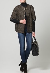 Tweed capejacka i grått och svart, med silverfärgade detaljer, korta ärmar och framknäppning. Matchas med mörka jeans och en svart handväska.