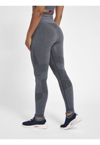 Szare legginsy wykonane z elastycznego materiału z teksturowanym wzorem o różnych motywach i liniach, zestawione z granatowymi butami sportowymi.